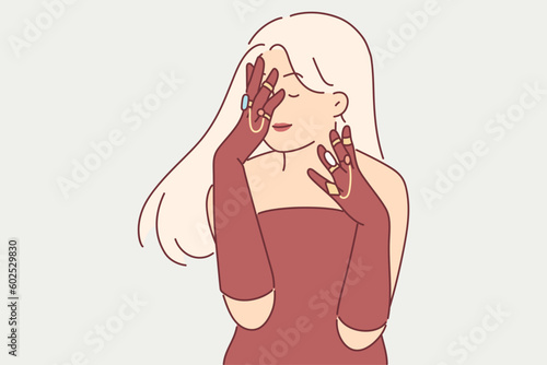 Elegant woman in evening dress covers face with hands, wanting to show off gold rings and jewelry