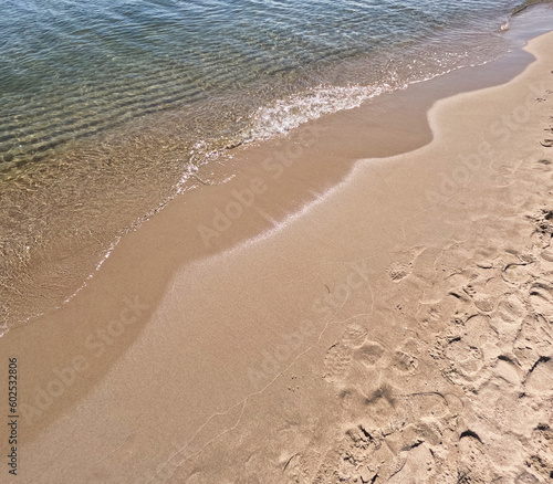 Waves on the beach. Moving background with rippling water on the seashore. Sand on the beach flooded with water.