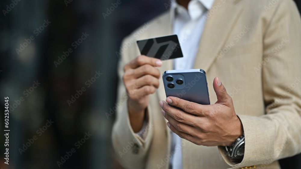 Modern businessman holds credit card and using smartphone. Banking, finance, online payment, e commerce Modern businessman holds credit card and using smartphone. Banking, finance, online payment, e commerce