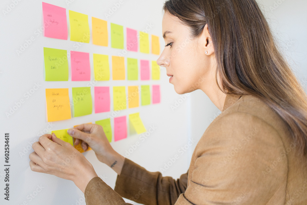 Female Entrepreneur Organizing Tasks with Post Its on the Wall Feeling Happy, Optimistic and Productive