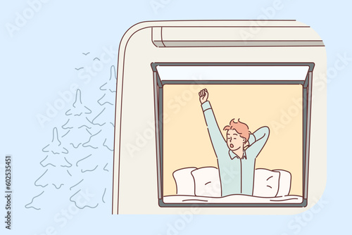 Man tourist wakes up in RV van parked near forest and yawns sitting in bed raising hand up