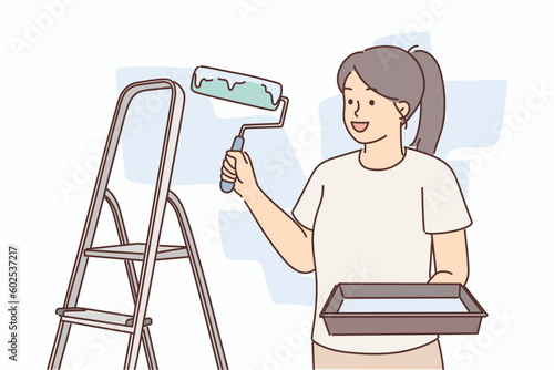 Woman molar with roller for painting walls stands near ladder making repairs in apartment
