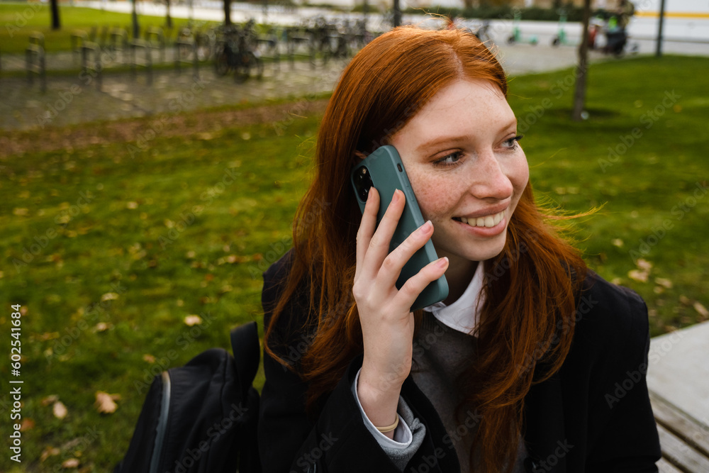 Smiling woman talking on mobile phone while sitting on bench in park Smiling woman talking on mobile phone while sitting on bench in park