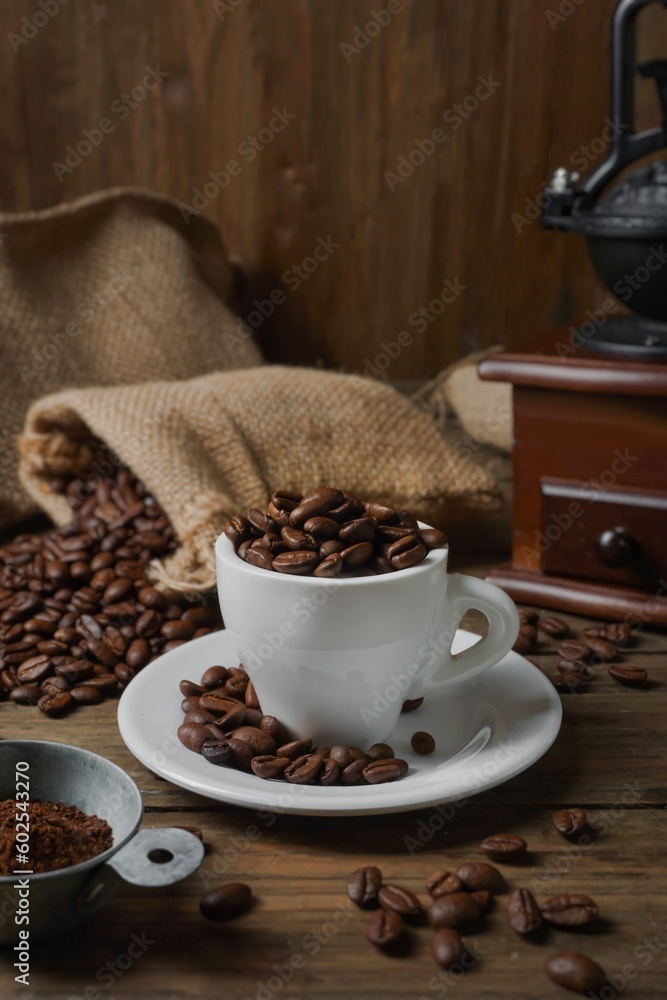 Roasted coffee beans in a cup, coffee beans in a sack, and a coffee grinder