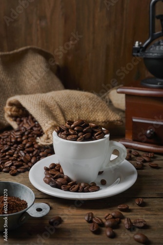 Roasted coffee beans in a cup, coffee beans in a sack, and a coffee grinder