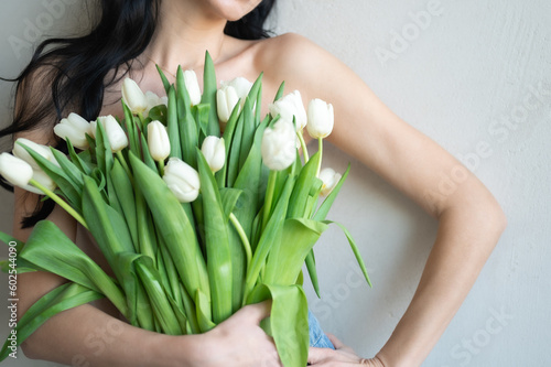 Woman with naked shoulders holding white tulips isolated on grey background with copy space