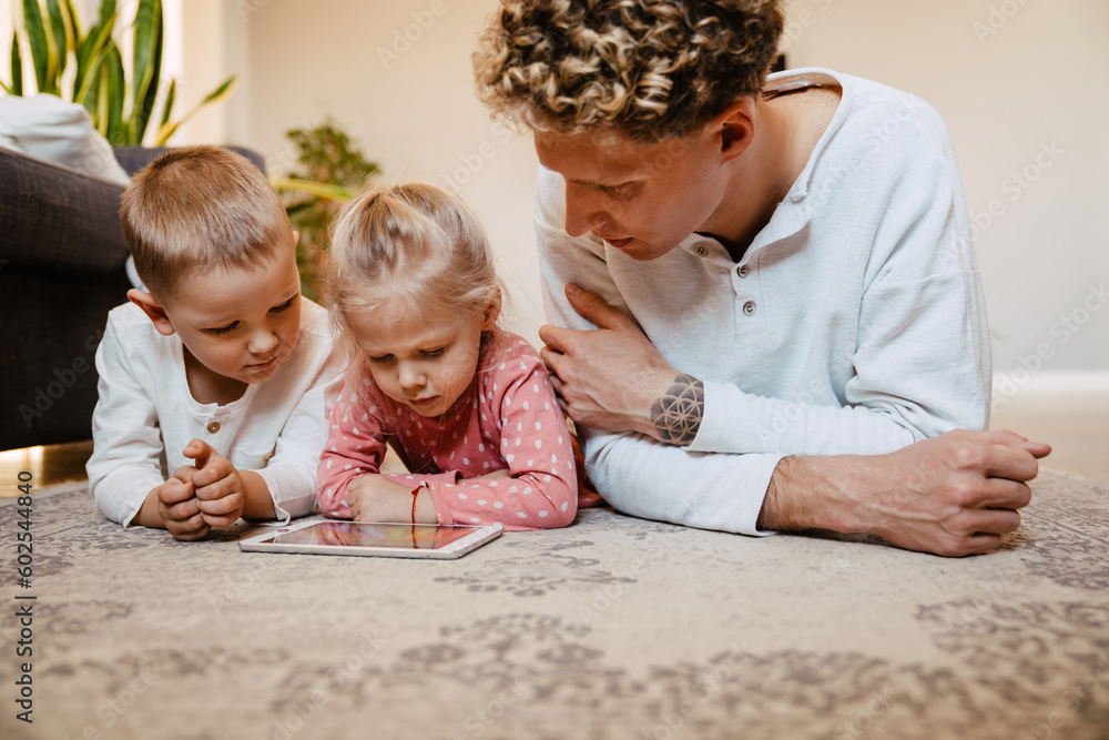 Father and his kids watching cartoons on tablet while laying on floor at home Father and his kids watching cartoons on tablet while laying on floor at home