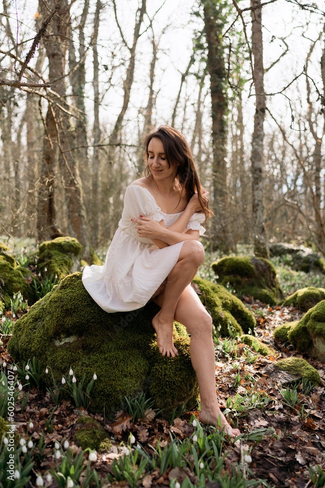 Portrait of a woman in the forest. She is sitting in a white dress on a meadow with snowdrops in a spring forest Portrait of a woman in the forest. She is sitting in a white dress on a meadow with snowdrops in a spring forest