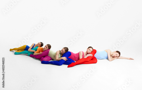Artistic performance. Young girls, ballet dancers in multicolored bright clothes dancing, lying on floor against grey studio background. Concept of creativity, classic dance style, contemporary art