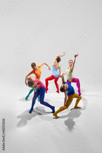 Group of talented, artistic female ballet dancers in bright, multicolored clothes performing against grey studio background. Concept of beauty, creativity, classic dance, elegance, contemporary art