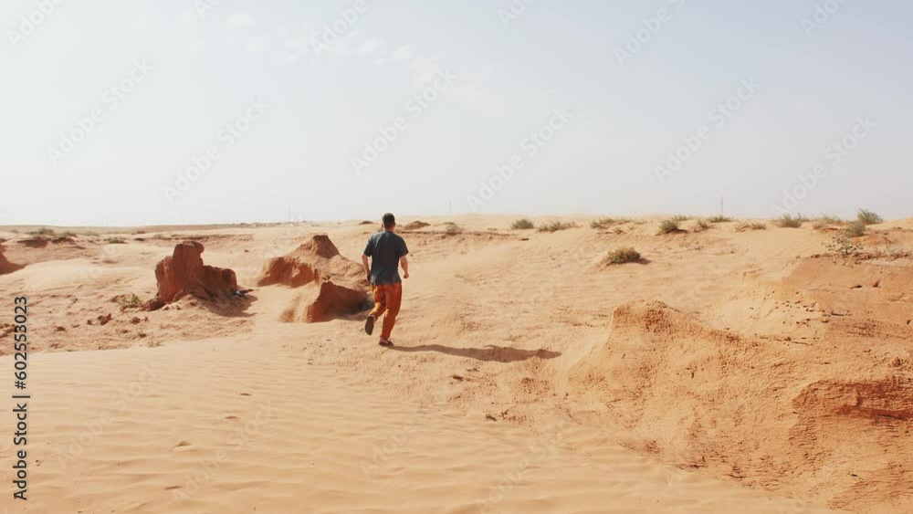 Young man travels and runs on sand in desert with clay stones and sparse vegetation. Back view. Slow motion Young man travels and runs on sand in desert with clay stones and sparse vegetation. Back view. Slow motion