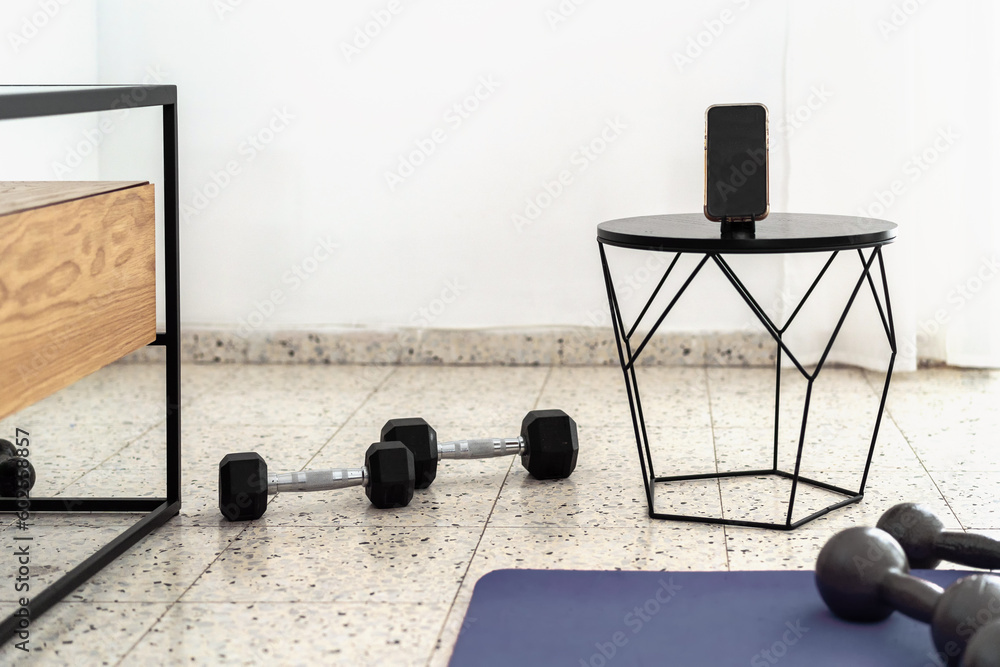 Online Fitness Training at Home: Dumbbell Workout with Phone on Stand and Yoga Mat on Floor. Mockup with White Isolated Screen.