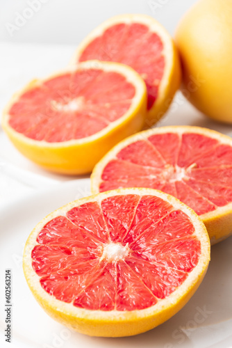 Close-up of split red grapefruits on plate and white tablecloth, vertical