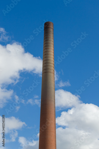 Old factory pipe. Brick chimney. Blue sky with clouds at the background.