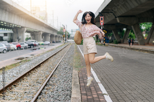 Young asian woman traveler jumping beside railway train station in Bangkok. Journey trip lifestyle, world travel explorer or Asia summer tourism concept.
