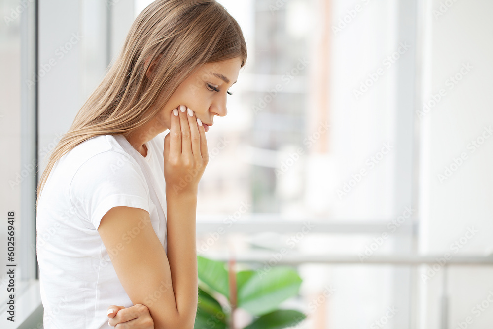 Woman suffering from toothache and touching her cheek while sitting at her desk Woman suffering from toothache and touching her cheek while sitting at her desk