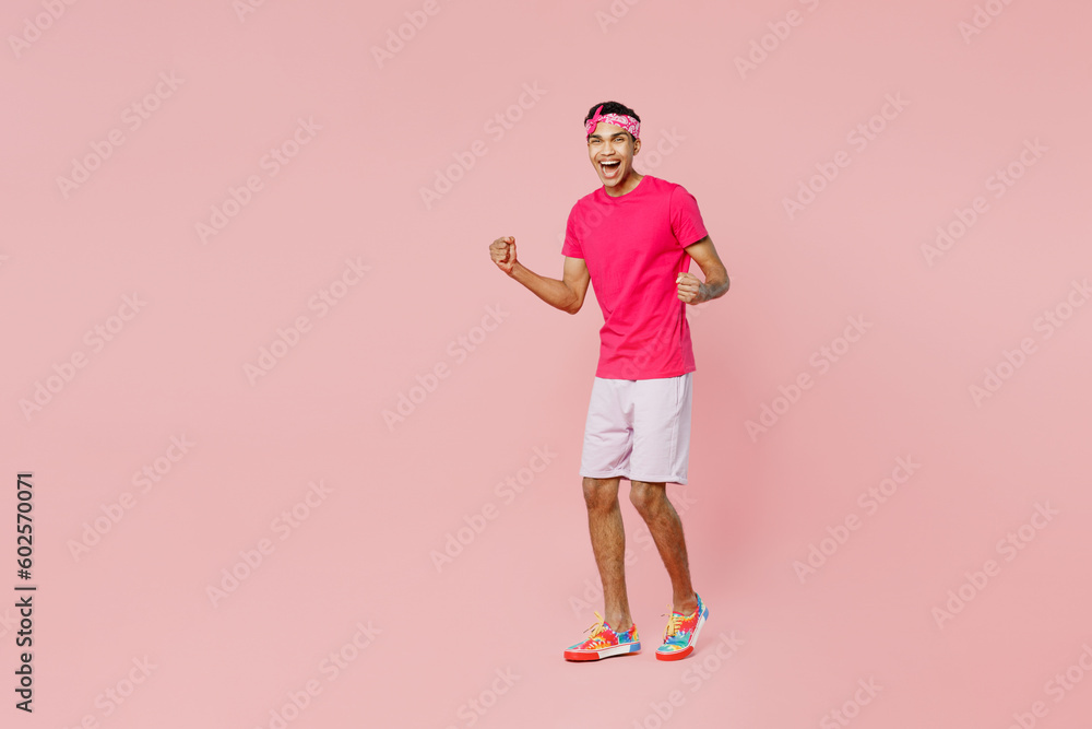 Full body young man of African American ethnicity he wear headscarf t-shirt casual clothes doing winner gesture celebrate clenching fists say yes isolated on pastel plain light pink color background. Full body young man of African American ethnicity he wear headscarf t-shirt casual clothes doing winner gesture celebrate clenching fists say yes isolated on pastel plain light pink color background.
