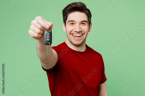 Young overjoyed man he wears red t-shirt casual clothes hold in hand car fob keyless system stretch hand to camera isolated on plain pastel light green background studio portrait. Lifestyle concept.