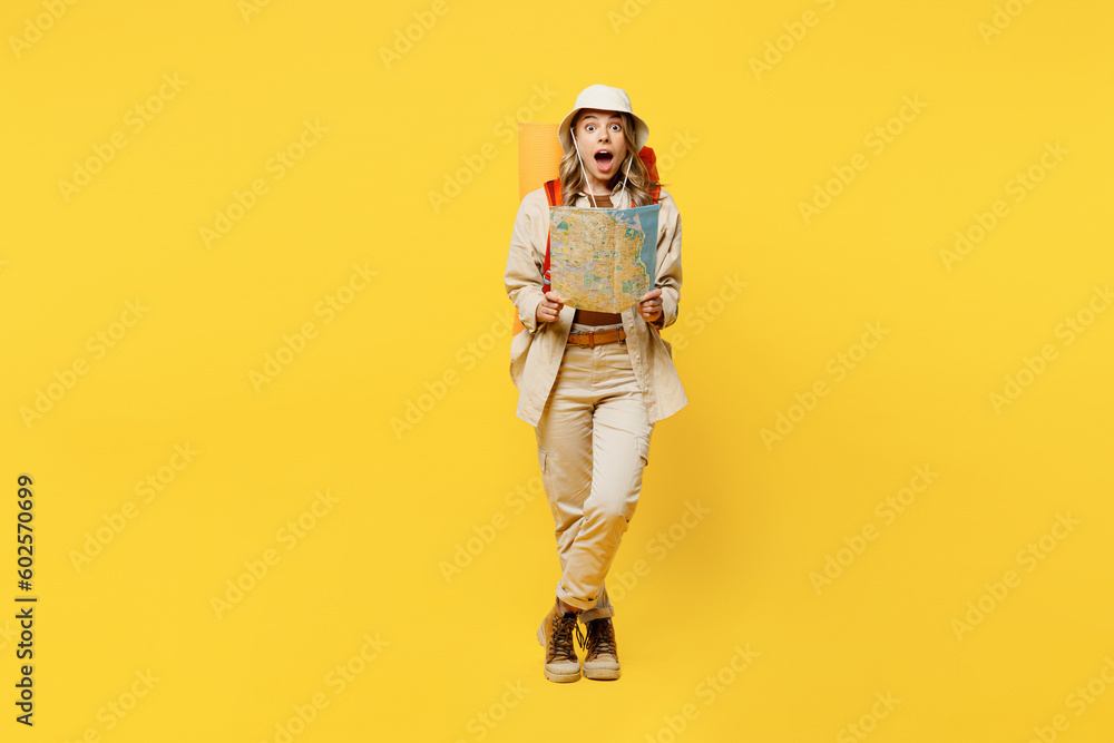 Full body amazed impressed young woman carry bag with stuff mat reading map isolated on plain yellow background. Tourist leads active lifestyle walk on spare time Hiking trek rest travel trip concept - obrazy, fototapety, plakaty 