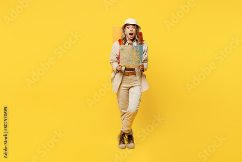 Full body amazed impressed young woman carry bag with stuff mat reading map isolated on plain yellow background. Tourist leads active lifestyle walk on spare time Hiking trek rest travel trip concept