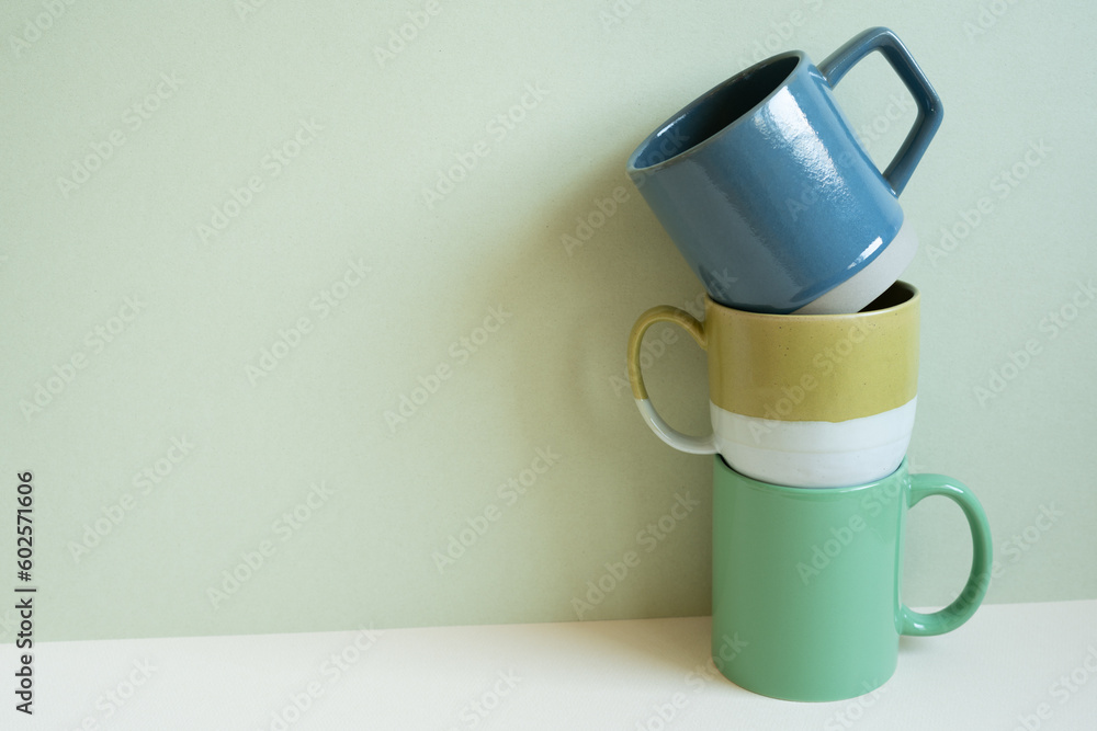 Stack of blue and green mug cups on white table. mint wall background. copy space