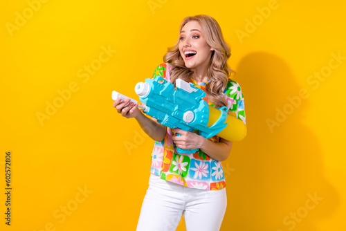 Photo of excited pretty woman dressed flower print t-shirt shooting water gun empty space isolated yellow color background