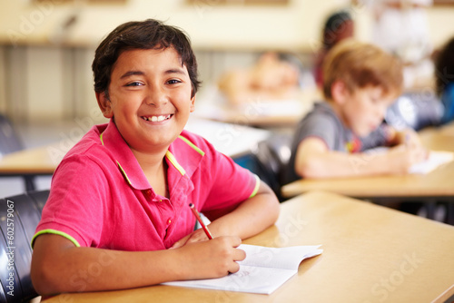 Education, learning and portrait of kid in classroom, smile and writing in book at Montessori school. Happy face, students at desk in class and studying, child development and kids in study or test.