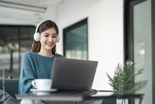 Young woman in modern headphones sit on couch in living room work on laptop