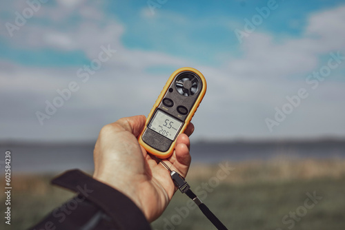 Person holding modern digital anemometer outdoors for measuring wind speed, temperature, humidity and other atmospheric effects. photo