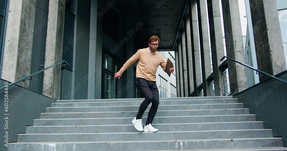Happy young man actively dancing while walking down the stairs. Cheerful man walks on stairs outside his office, starts funny victory dance celebrating. - obrazy, fototapety, plakaty 