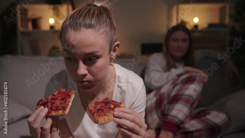 Young woman with bulimia eating pizza at night. Sister or friend warning about overeating