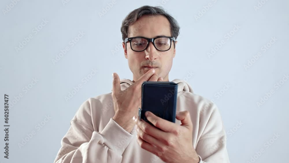 An adult man in glasses and a light hoodie works on a smartphone on a white background An adult man in glasses and a light hoodie works on a smartphone on a white background