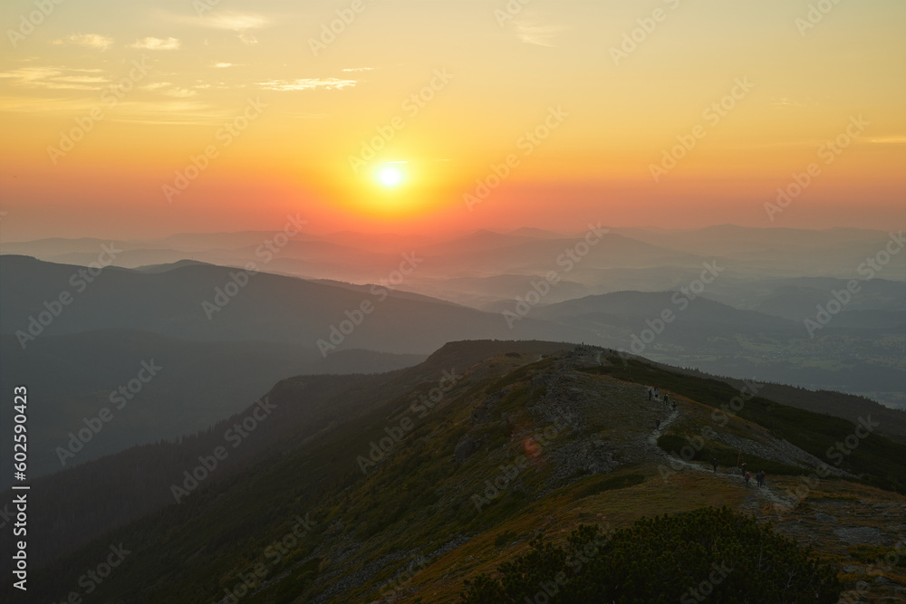 Sunrise in mountains. Natural mountain landscape with illuminated misty peaks, foggy slopes and valleys, blue sky with orange yellow sunlight