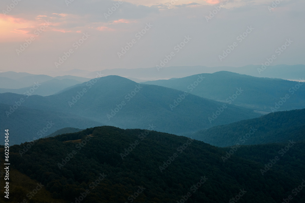 Sunset in mountains. Natural mountain landscape with illuminated misty peaks, foggy slopes and valleys, blue sky with orange yellow sunlight