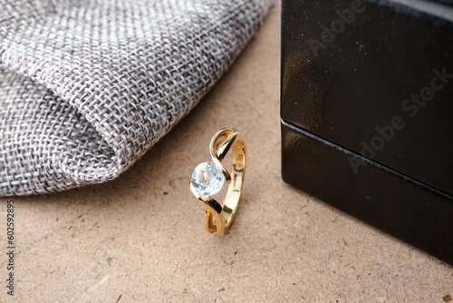 Gold wedding rings on a wooden pattern plinth and black ringbox behind with burlap trim	 photo