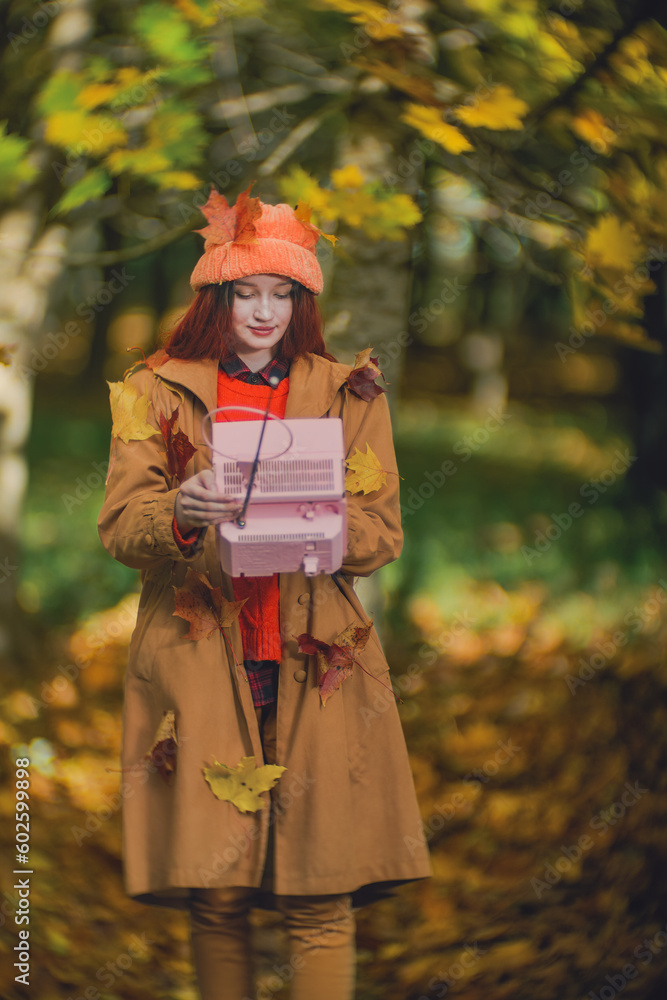 Young hipster woman in an orange hat with a retro TV in her hands in the park in the fall Young hipster woman in an orange hat with a retro TV in her hands in the park in the fall
