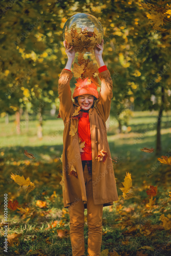 Happy young woman tosses maple leaves up in park in fall