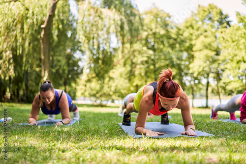 Close-up of group of women exercising during outdoors fitness class in park. Plank exercise for abs muscle.