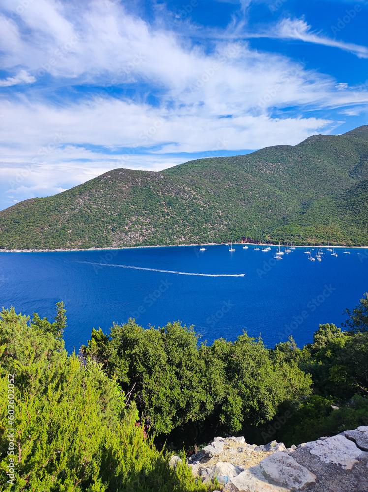 This stunning aerial view showcases the vivid blue Mediterranean Sea with boats, framed by mountains, and enveloped in lush trees. Embrace nature's captivating harmony. The essence of Greek tourism.