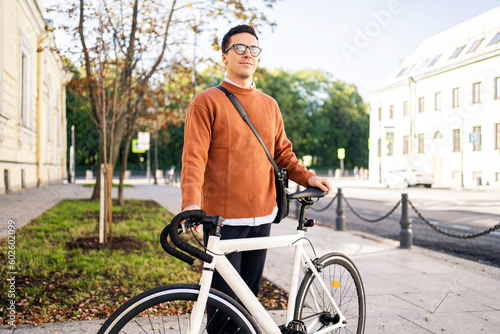 A happy cyclist is a young guy and a white bike riding to work in formal clothes.