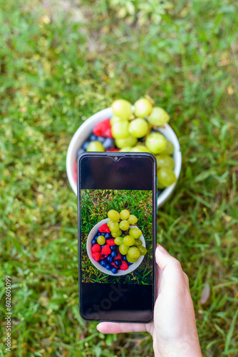 Miseczka wypełniona owocami maliny, borówki i winogrona, fotografowana za pomocą telefonu komórkowego.