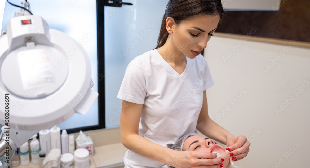 Beautician using cotton discs to clean the skin of young female client at beauty salon.