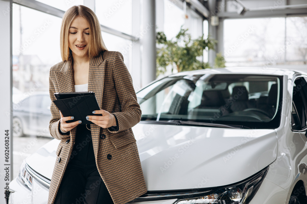 Saleswoman in car showroom standing by car holding tablet