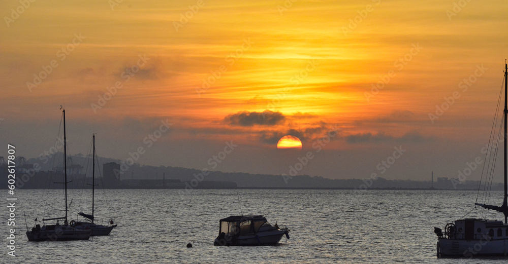 A boat sails as the sun sets, on the beach off the coast in Uruguay, Montevideo with a beautiful golden yellow and orange light