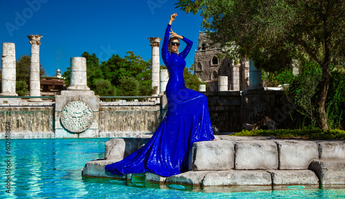 Elegant luxury evening fashion. Glamour, stylish elegant woman in blue long evening gown dress is posing nead the pool in luxury hotel outdoor. Female model in amazing long dress. photo