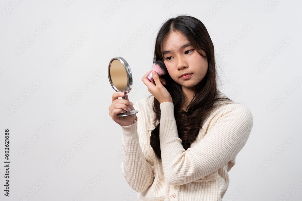 Beautiful young woman makes blush on her face using makeup brush on isolated white background. Teenage girl doing her own makeup. Close up portrait. Copy, empty space for text Beautiful young woman makes blush on her face using makeup brush on isolated white background. Teenage girl doing her own makeup. Close up portrait. Copy, empty space for text