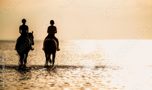 Two horse riders in the ocean at the sunset. Equestrian theme.