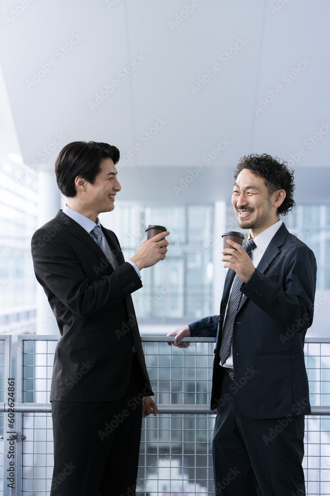 Two happy business men in suits conversing over coffee during break,width copy space vertical Two happy business men in suits conversing over coffee during break,width copy space vertical