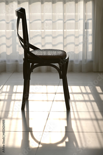 An old wooden chair and a shadow stand by a window with white curtains.