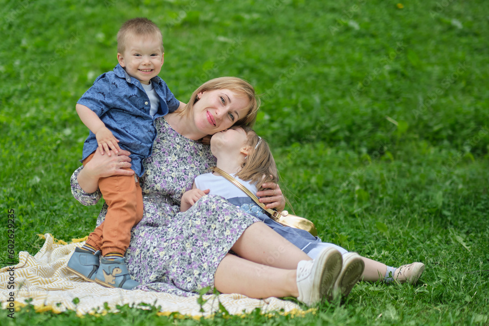 Cherished memories: A woman in her middle years lovingly holds her children close as they sit on a blanket in the park, creating lasting memories together. Cherished memories: A woman in her middle years lovingly holds her children close as they sit on a blanket in the park, creating lasting memories together.